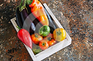 White box with vegetables on a rusty background. Aubergines, bell pepper, tonatoes.