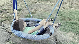 White boy swinging in a web swing in the playground