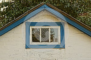 White brick attic of a rural house with a small blue window