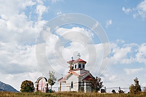 White brick church with a red roof in a field with a metal fence