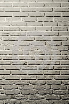 White brick wall of a warm shade lit from above by a lamp. White brick wall, perfect as a background, square photograph