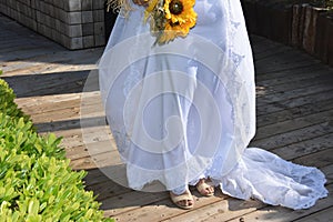 white bride dress, legs in sandals on the grass, yellow flowers