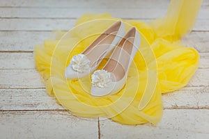 White bride`s shoes with floral decor stay on yellow airy fabric.