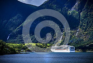 A white bright cruise-ship arrives at a fjord village in norway.