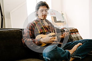 White bristle man playing ukulele while resting on couch