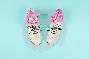 White brogue shoes filled with pink daisies and wildflowers on pastel blue background