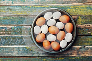 White and brown chicken eggs in vintage bowl on rustic wooden table from above. Organic and farm food.