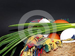 White and brown eggs and a bunch of green onions on a checkered napkin in a bowl on a black background