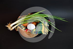 White and brown eggs and a bunch of green onions on a checkered napkin in a bowl on a black background