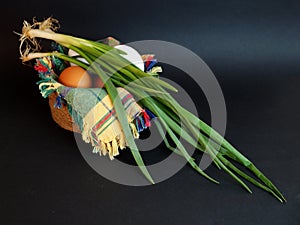 White and brown eggs and a bunch of green onions on a checkered napkin in a bowl on a black background