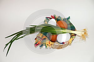 White and brown eggs and a bunch of green onions on a checkered napkin in a bowl on a white background