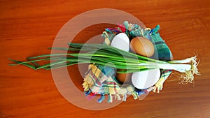 White and brown eggs and a bunch of green onions on a checkered napkin in a bowl on a wooden table