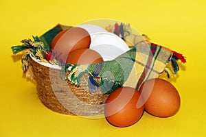 White and brown eggs and a bunch of green onions on a checkered napkin in a bowl on a yellow background