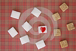 White and brown sugar cubes with a red heart on one of them. Top view. Diet unhealty sweet addiction concept photo