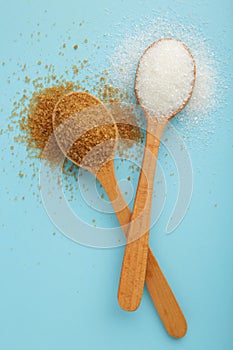 White and brown sugar in wood spoon on blue background