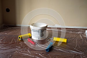 White bucket with paint and wallpaper rollers on the background of oilcloth on the floor. Room repair photo