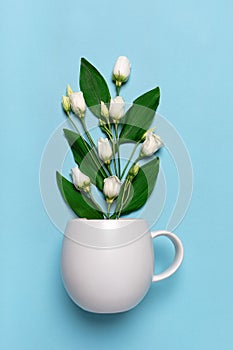 White bud eustoma flower in tea coffee cup mug close-up. Vertical studio shot on blue background. Concept of spring, greenery,