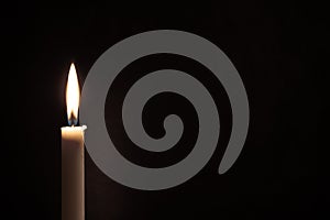 White burning candle on a black background. Mourning, burning candle