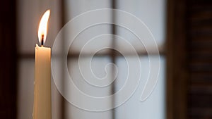 White burning candle on a blurred background of window