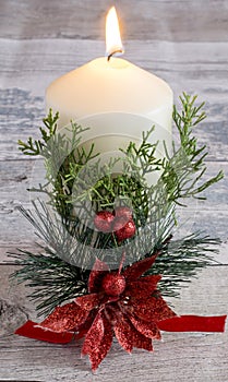 White burning candle with holly flower and green branch