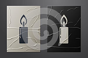 White Burning candle icon isolated on crumpled paper background. Cylindrical candle stick with burning flame. Paper art