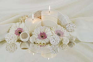 White burning candles with white greber daisy flowers reflecting in a mirror