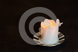 White burning pillar candle standing on gold decorated saucer on dark dining table