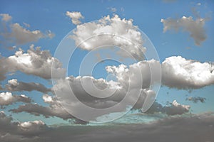 White bushy and fluffy clouds In the blue sky, with deep dark shadows on their bottoms from low layer of cloudiness.