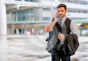 White business man holds the bottle of water and hand his suit or jacket on his arm, also use mobile phone to communicate with