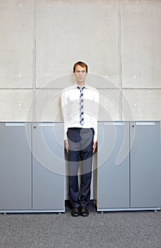 White business man standng straight between cabinets in office