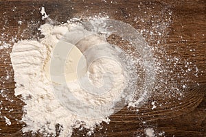 White butter or margarine in the shape of a heart in flour on a wooden table.
