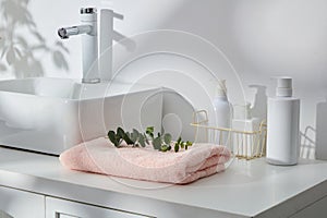 White cabinet displayed wash basin, folded towel and several unbranded pump bottles. Mockup bottle for skin care cosmetic