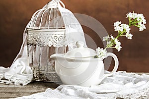 White cage and a tea pot with flowers and decoration on a wooden table