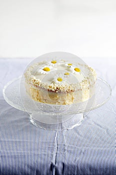 White cake on a cake stand with daisy flowers and almonds