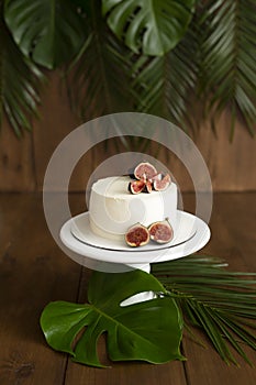 White cake with figs on a wooden stand. Tropics