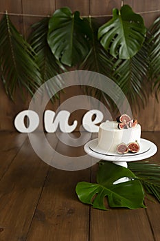 White cake with figs on a wooden stand. Tropics. Letters one