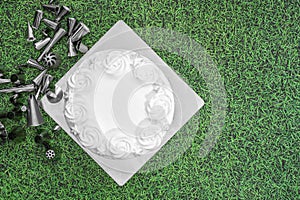 White cake frosting with baking accessories piping nozzles flat lay on green grass background