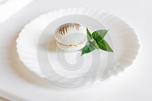 A white cake lies on a white plate on a light background. Light macaroons. Delicious pastries