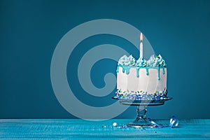 White cake with one lit birthday candle on a blue background