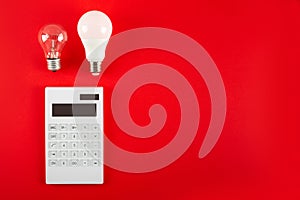 White calculator and incandescent lamp or LED bulb on red background. Concept showing the payment of electricity bills. The