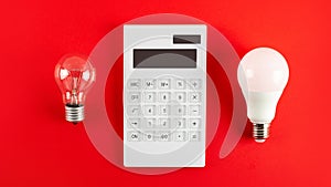 White calculator and incandescent lamp or LED bulb on red background. Concept showing the payment of electricity bills. The