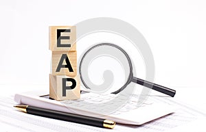 On a white calculator, next to a magnifying glass and a black pen, wooden cubes marked EAP Employee Assistance Program stand