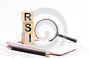 On a white calculator, next to a magnifying glass and a black pen, wooden cubes marked RSI Relative Strength Index