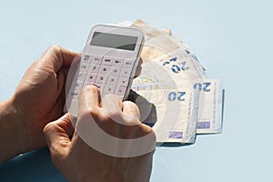 A white calculator in a woman`s hand and euro banknotes on a blue background