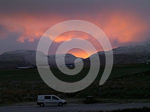 White camper van on the country road along the snow capped mountain range under beautiful sunset sky