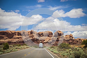 White camper van drives toward red rock formation at Arches National Park in Utah USA