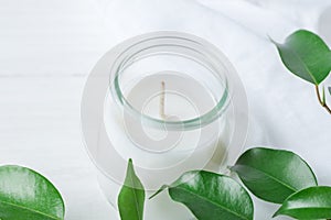 White Candle in Glass Jar Fresh Tree Branches with Tender Green Leaves on Wood and Cotton Linen Fabric Background