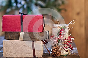 White candle holder decorated with pine cone and red ashberry and red, brown and sandy yellow Christmas gifts on wooden table