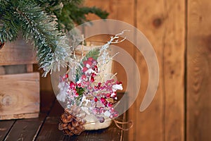 White candle holder decorated with pine cone and red ashberry under Christmas tree on wooden background