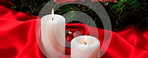 White candles on red satin burning on a dark background, banner
